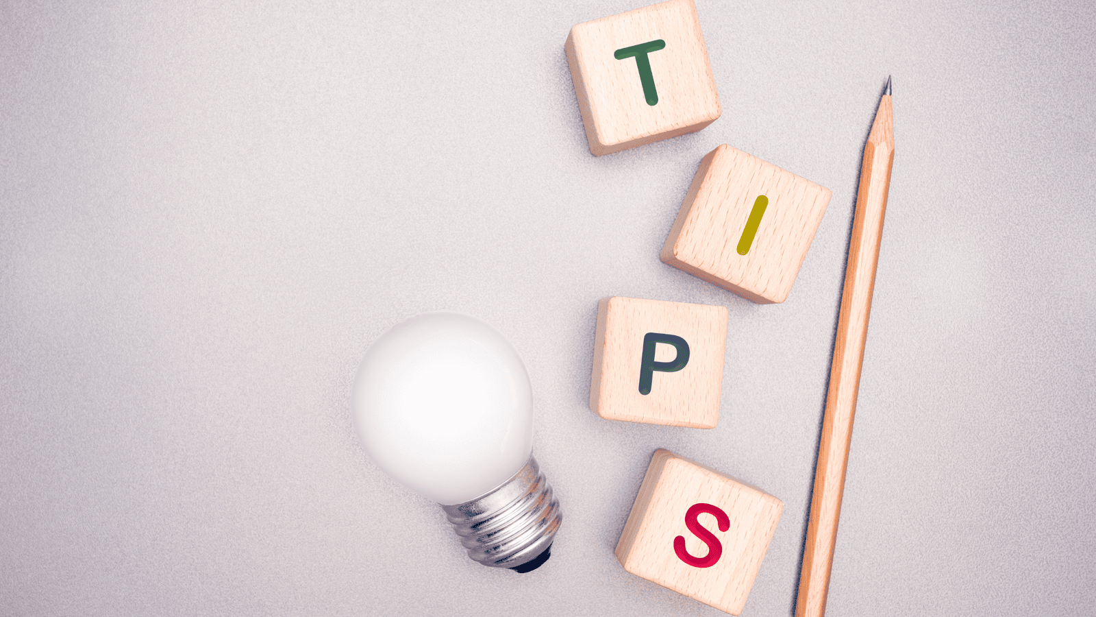 Light bulb, pencil, and wooden blocks spelling ‘TIPS’ representing practical ideas for staying organized with tax records, receipts, and filing documents for future Canadian tax seasons.