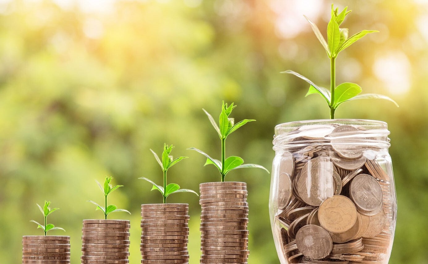 Close-up of stacked coins growing in height with small plants sprouting from each level beside a jar of savings, representing increasing financial responsibilities, income growth, and the need for proper financial planning.