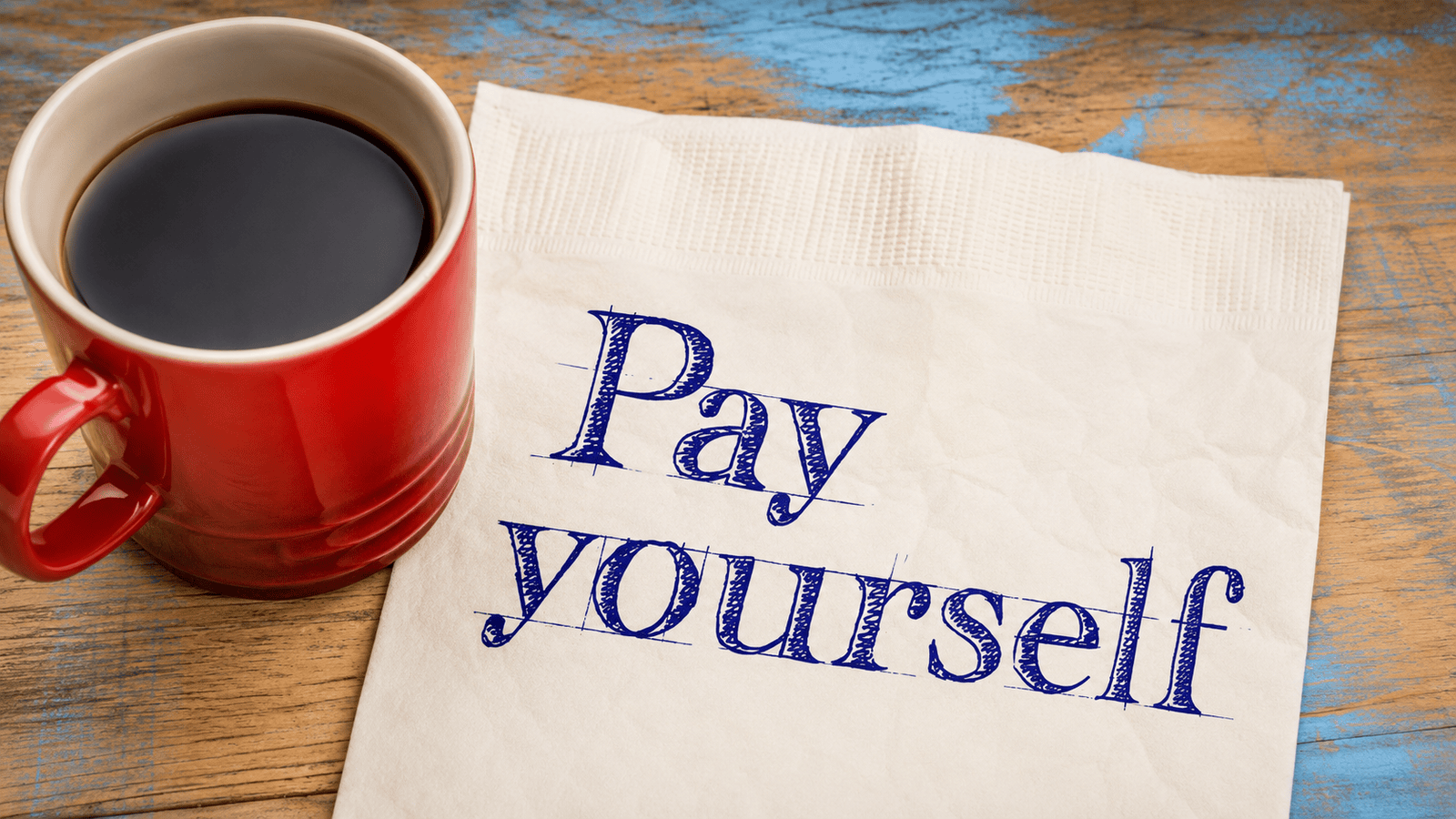 Red coffee cup beside a note reading ‘Pay yourself,’ representing the importance of creating a consistent owner compensation strategy based on business cash flow, profitability, and financial planning.