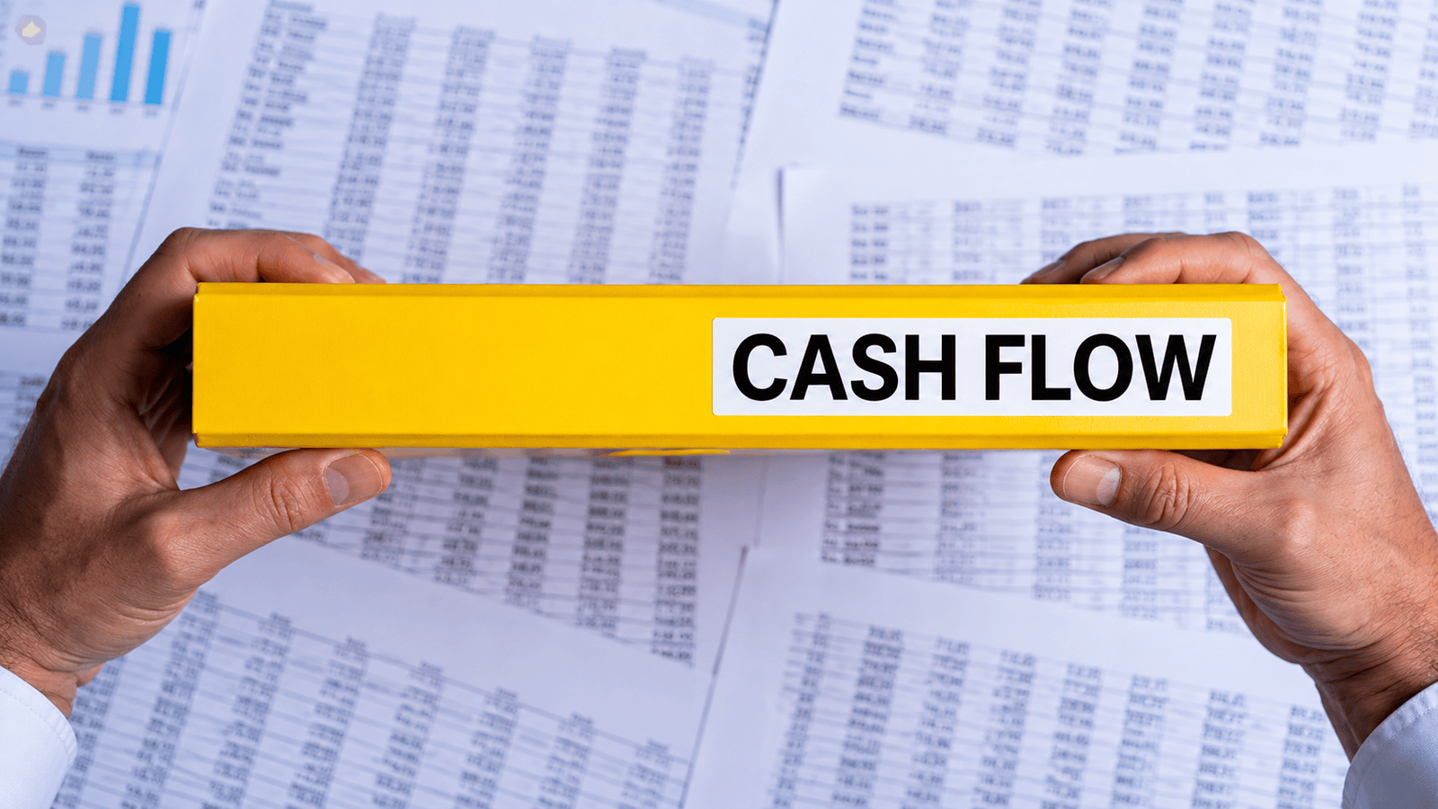 Hands holding a yellow binder labeled ‘Cash Flow’ over financial spreadsheets, representing the importance of liquidity, tax payment timing, and financial planning for Canadian businesses.