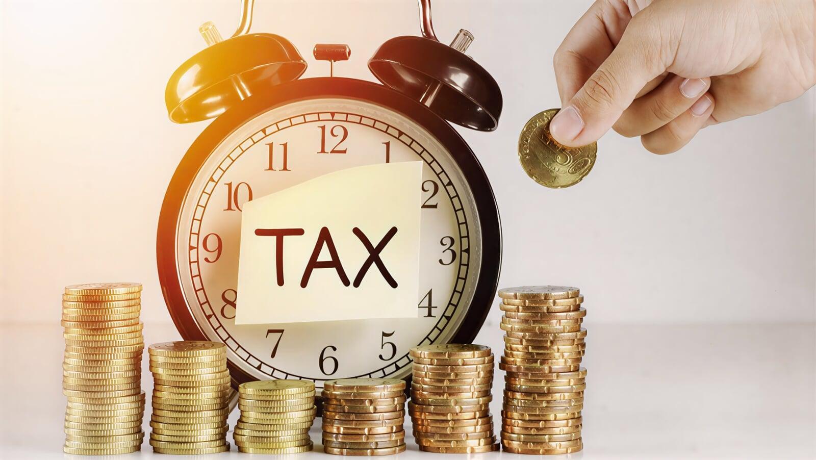 Tax installment concept showing alarm clock labeled ‘TAX’, stacks of coins, and hand placing money, representing periodic tax payments and CRA installment deadlines for Canadian businesses.