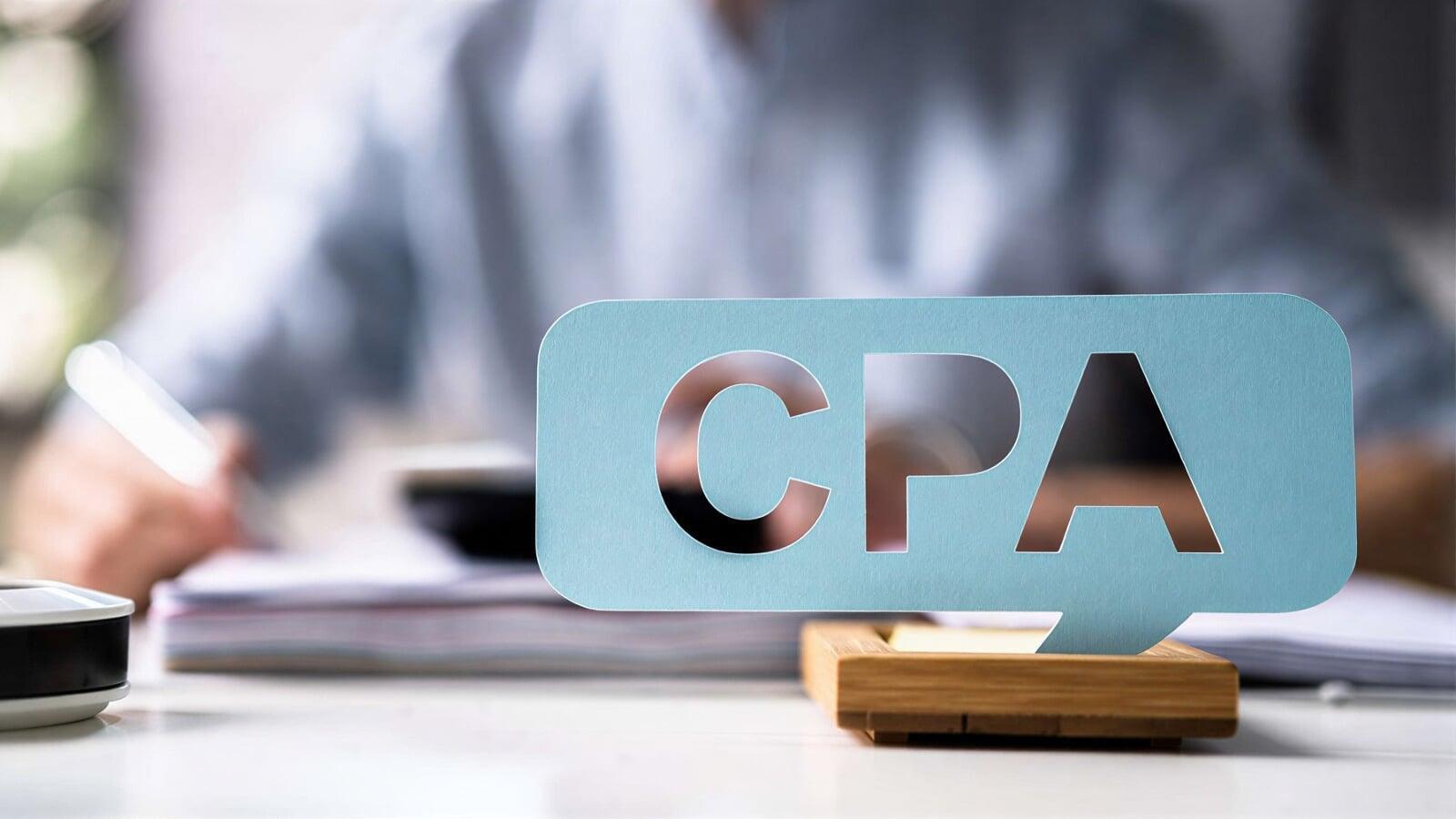 CPA sign displayed on an office desk with a professional working in the background, representing when businesses in London, Ontario should hire a CPA or accountant for tax planning and compliance support.