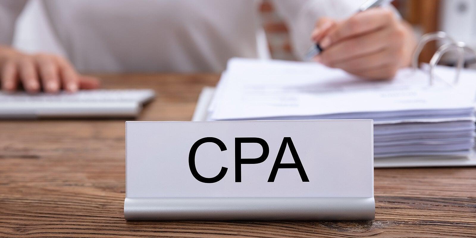 CPA nameplate on an office desk with documents and a professional working in the background, representing when businesses in London, Ontario should hire a CPA for tax planning and compliance support.