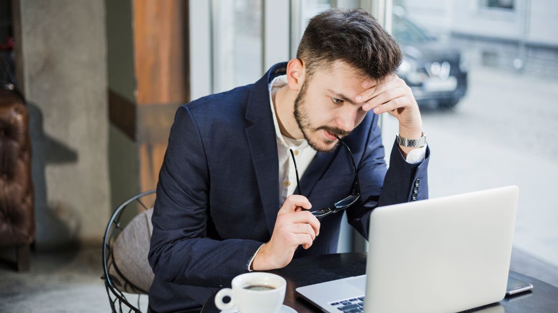 Close-up of a stressed entrepreneur working on a laptop with documents and coffee nearby, representing common mistakes business owners make when managing finances, operations, and decision-making in early stages.