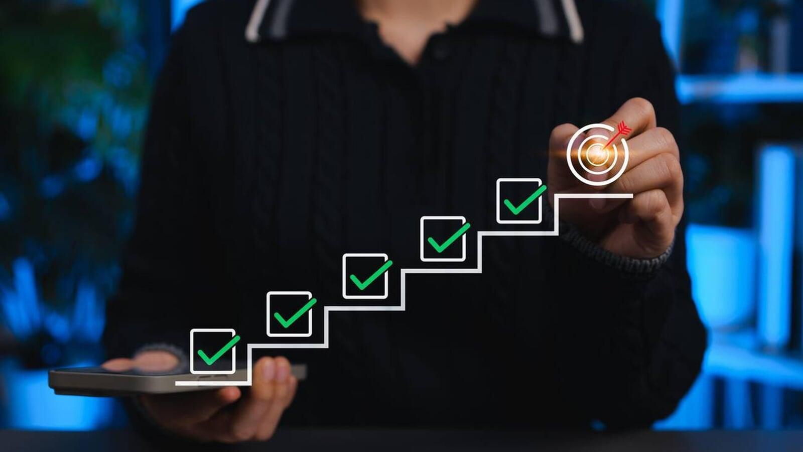 Person holding a smartphone and marking checkboxes along a step-by-step progress path leading to a target, representing a structured checklist to stay CRA-compliant before the April 30 tax deadline for businesses in London, Ontario.