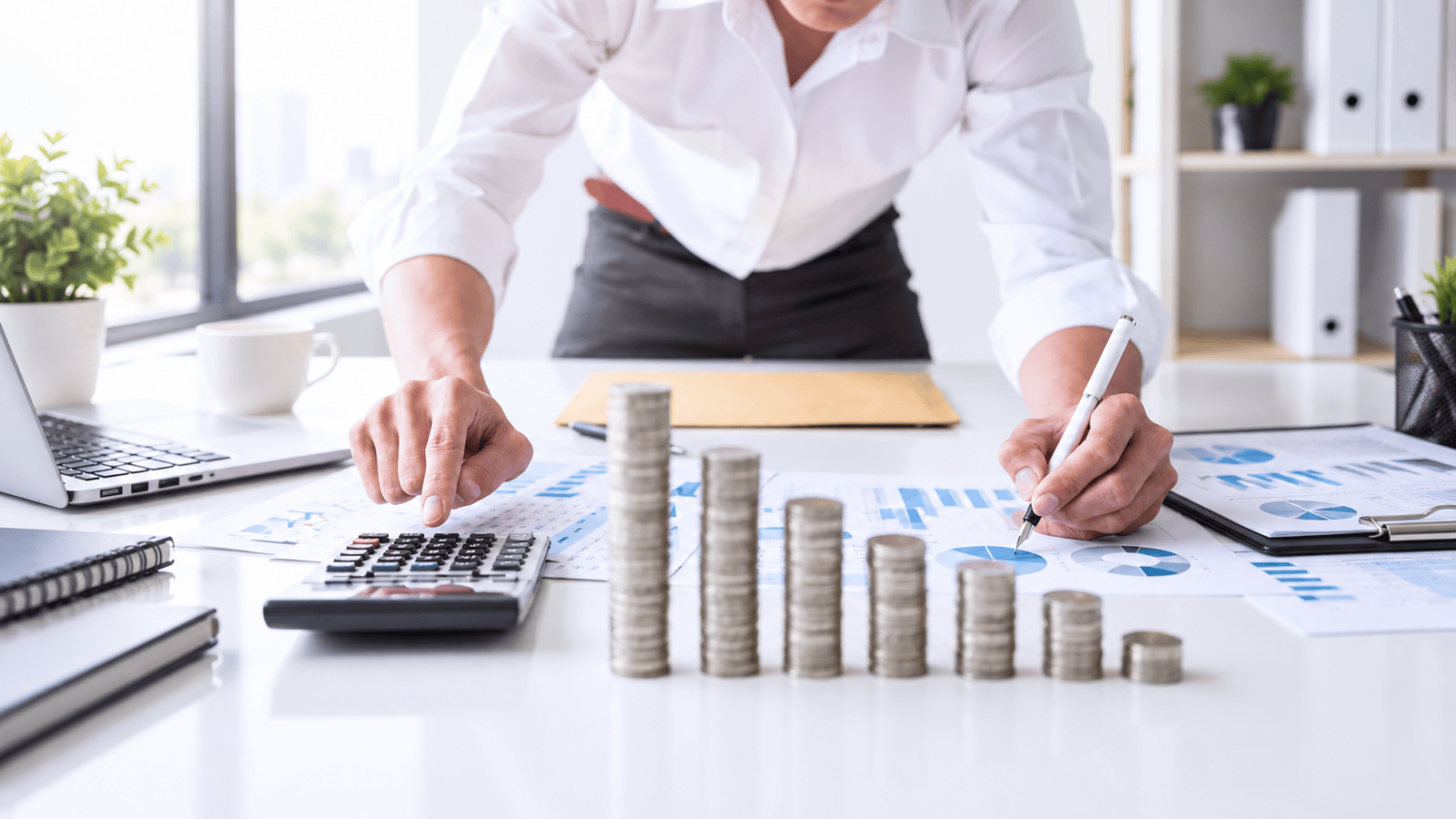 Business owner reviewing financial reports with a calculator and stacked coins, representing how an outdated accounting setup can create bookkeeping, payroll, and GST/HST problems for growing businesses in London, Ontario.