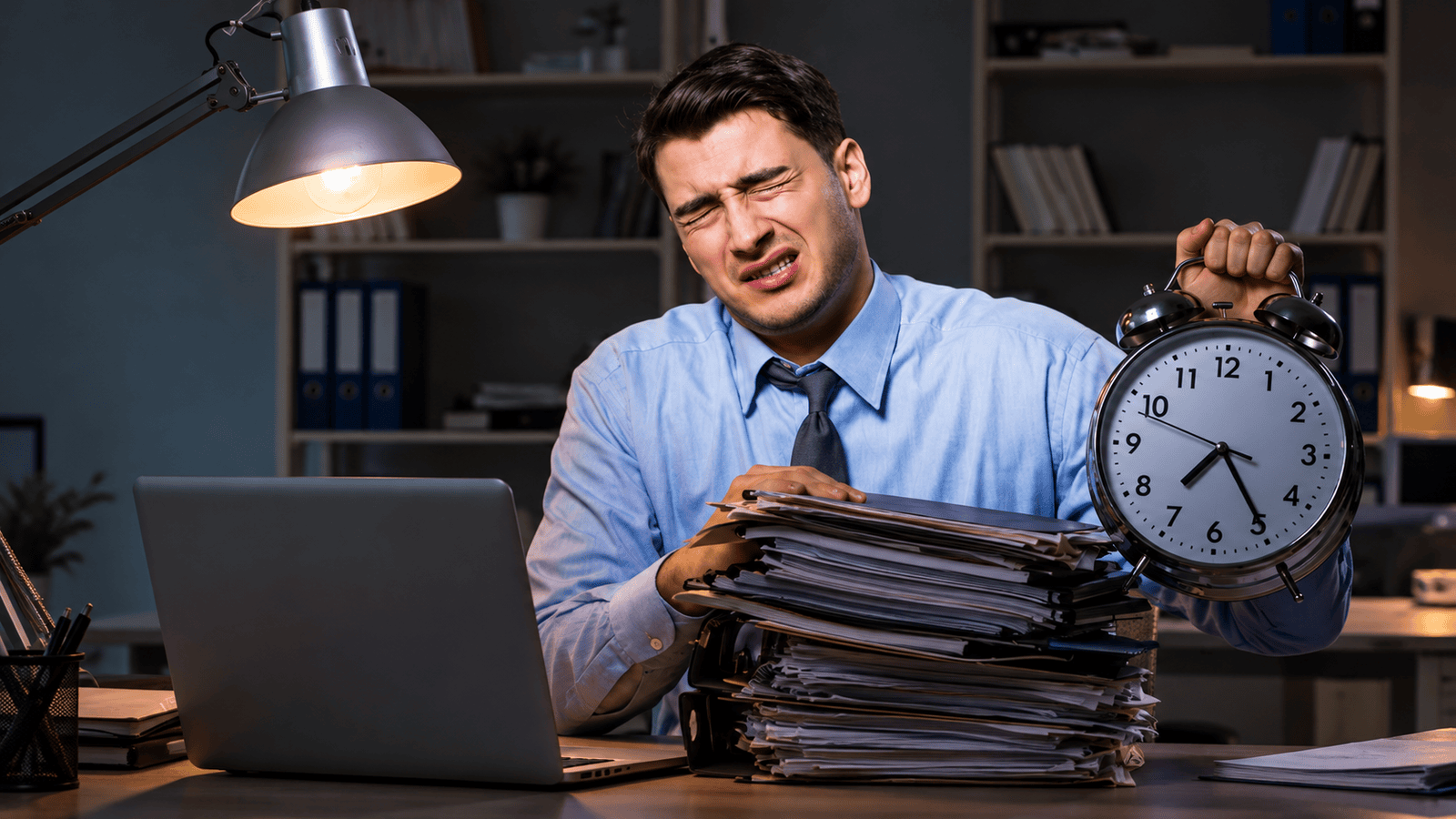 Stressed business owner sitting at a desk with stacks of paperwork, a laptop, and a large alarm clock, illustrating overdue corporate tax filings, CRA penalties, and mounting tax deadlines in Ontario, Canada.