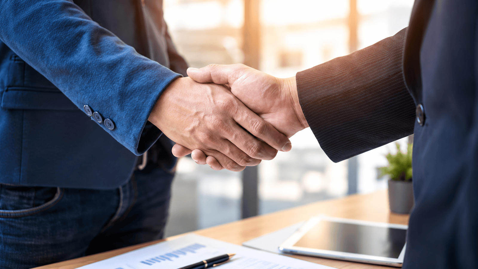Close-up of two business professionals shaking hands over a desk with documents and a tablet, representing the fair market pay test the CRA applies to family salaries in London, Ontario.