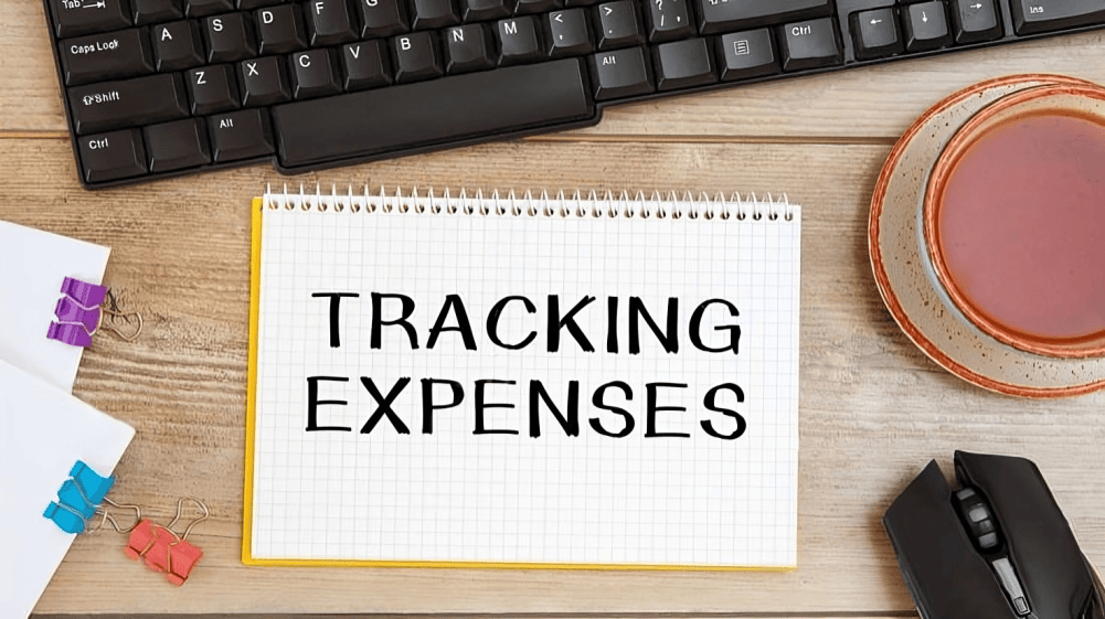 Notebook labeled “Tracking Expenses” beside keyboard, desk accessories, and coffee cup, representing expense tracking, bookkeeping improvements, and organized tax records for businesses in Ontario, Canada.