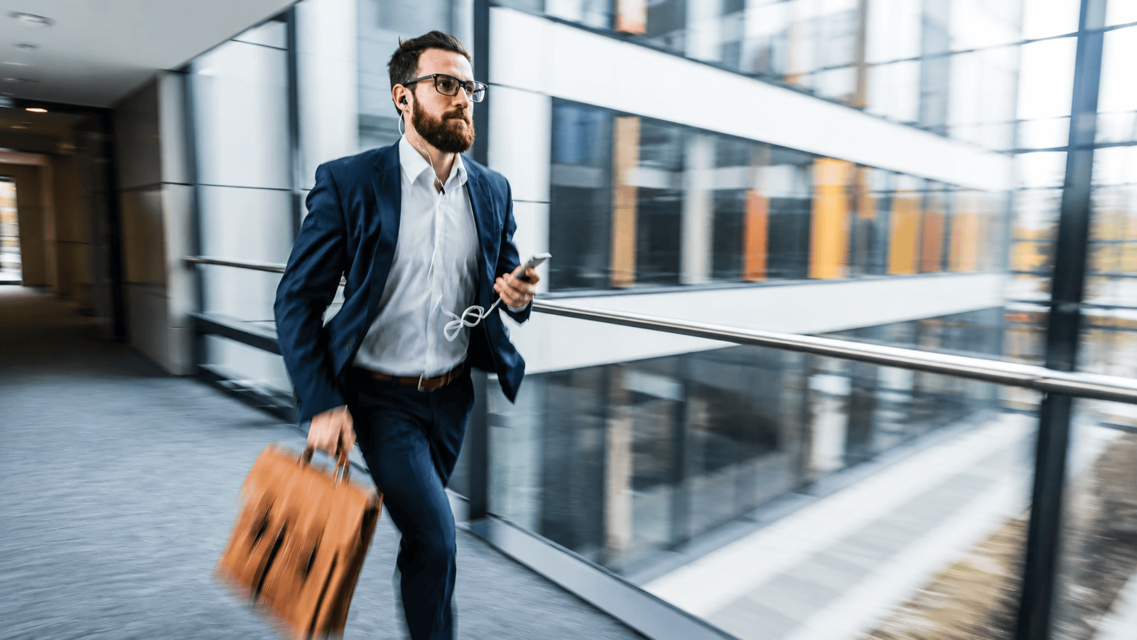 Motion-blurred professional rushing through a modern office building with a briefcase and smartphone, illustrating the constant hustle and founder dependency that often prevent small businesses from building scalable systems.