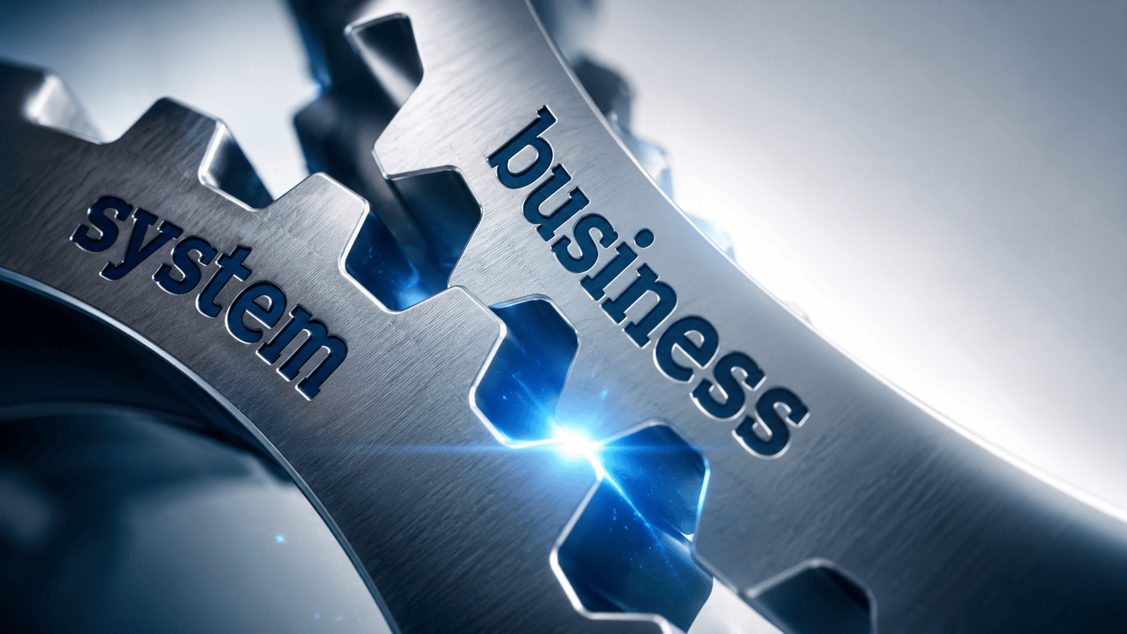 Close-up of two interlocking metal gears labeled "system" and "business," symbolizing how well-designed business systems work together to improve efficiency, consistency, and long-term organizational growth.