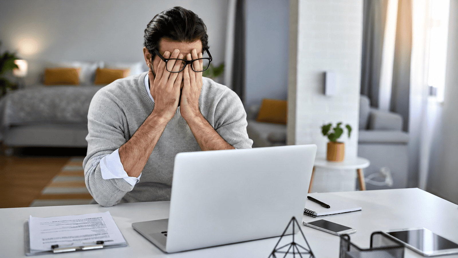 Business owner sitting at a home office desk with hands covering his face while looking at a laptop, illustrating founder burnout and the challenges of running a business without documented systems or delegation.