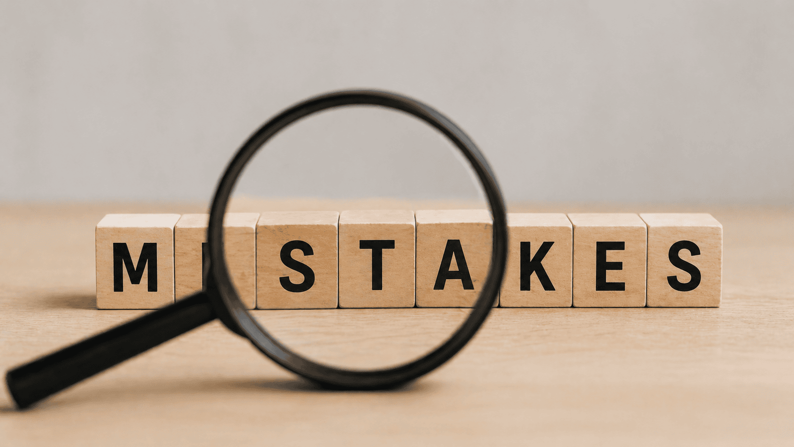 Close-up of wooden blocks spelling mistakes viewed through a magnifying glass on a desk, representing common errors and oversights business owners make when handling tax filings in Canada.