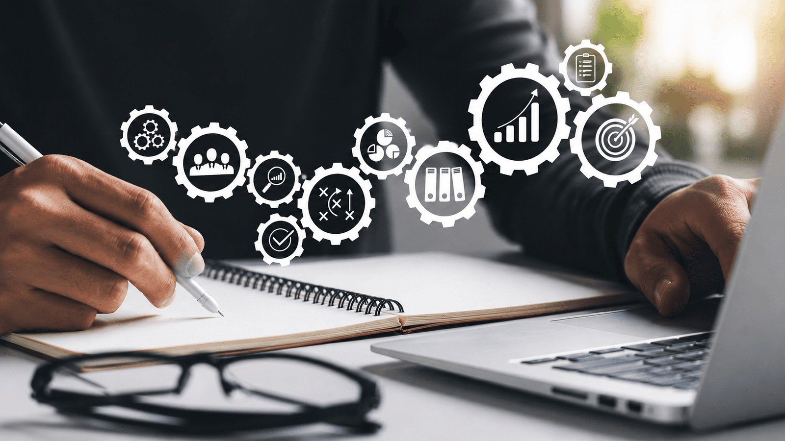 Close-up of a person working at a desk with a notebook and laptop, surrounded by floating business process icons representing systems, planning, delegation, organization, and growth, symbolizing the transition toward more structured business operations.