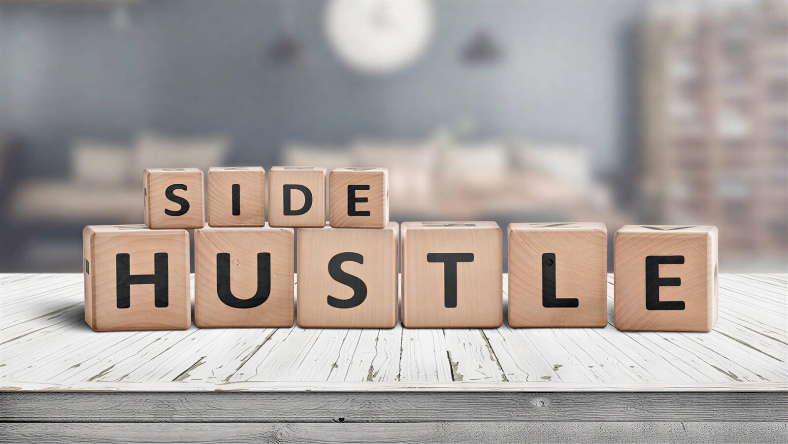 Close-up of wooden blocks arranged to spell “Side Hustle” on a desk, representing starting small income streams and the early stage of building a business idea from scratch.