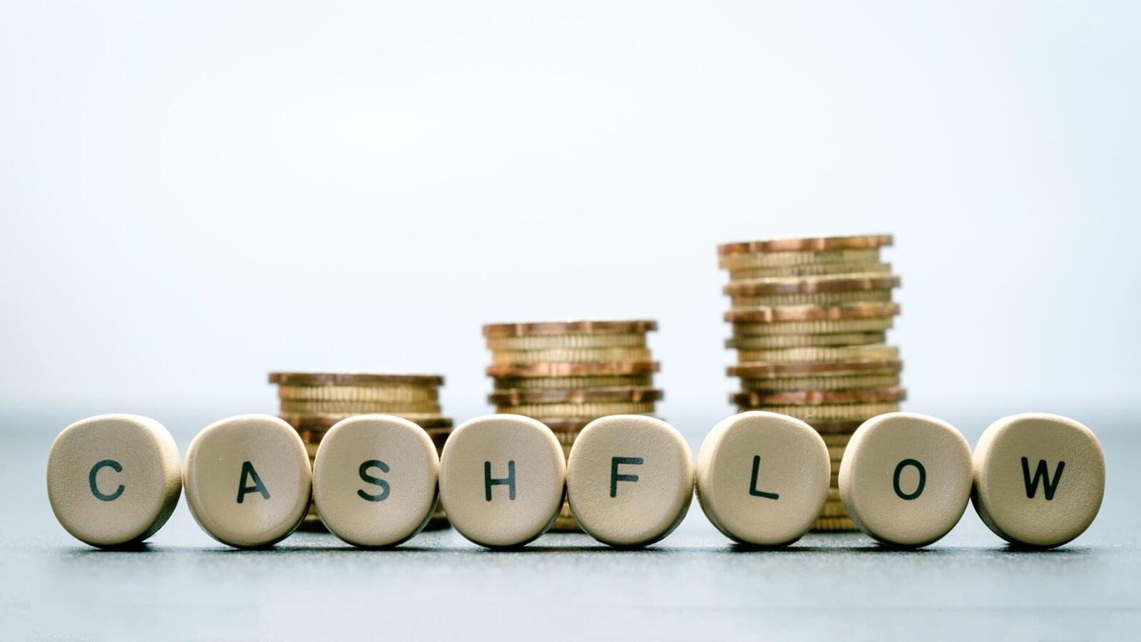 “Close-up of round letter tiles spelling ‘CASHFLOW’ placed in front of stacked coins, representing the movement of money in and out of a business and the financial awareness needed for sustainable growth.