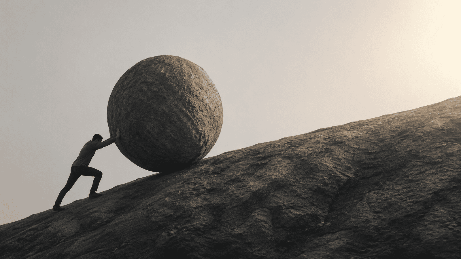 Conceptual image of a business professional pushing a massive stone uphill on a steep path, representing the unseen effort, persistence, and delayed progress often required before momentum begins to build.